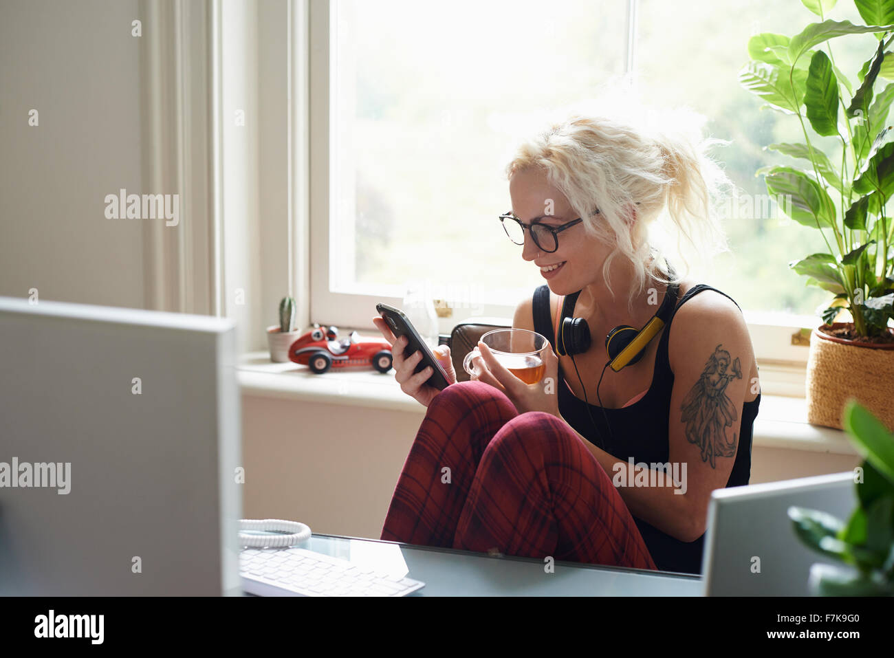 Jeune femme avec un casque et tattoo texting in home office Banque D'Images