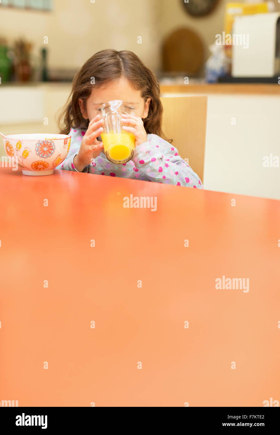 Girl drinking orange juice à table de petit déjeuner Banque D'Images
