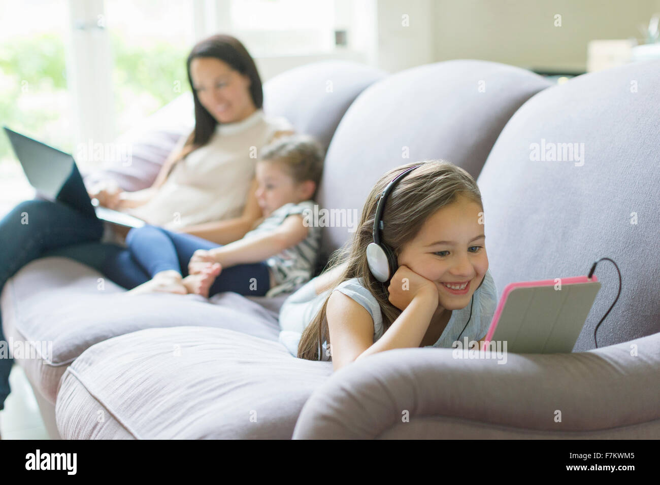 Fille avec écouteurs et tablette numérique portant sur le sofa du salon Banque D'Images