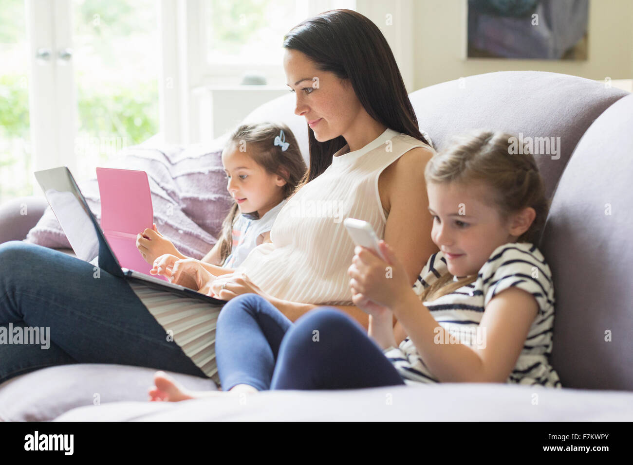 La mère et les filles avec un ordinateur portable, téléphone portable et tablette numérique sur canapé Banque D'Images