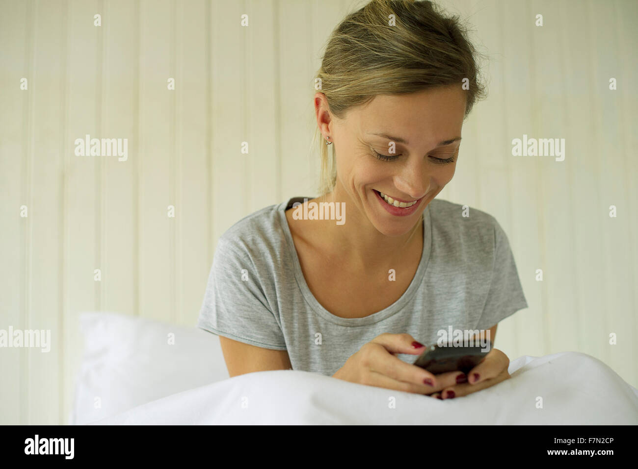 Femme assise au lit texting Banque D'Images