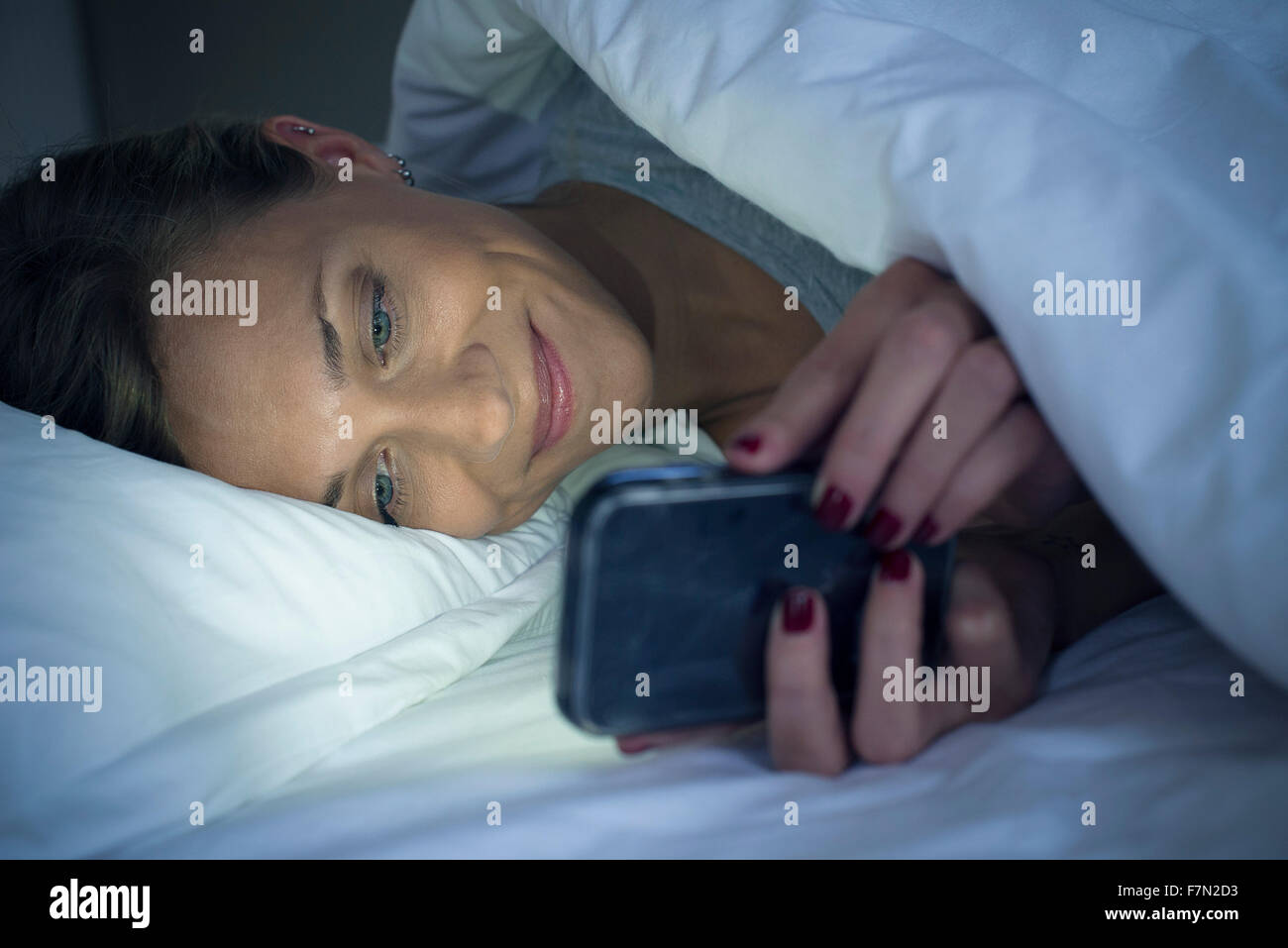 Woman Lying in Bed using smartphone Banque D'Images