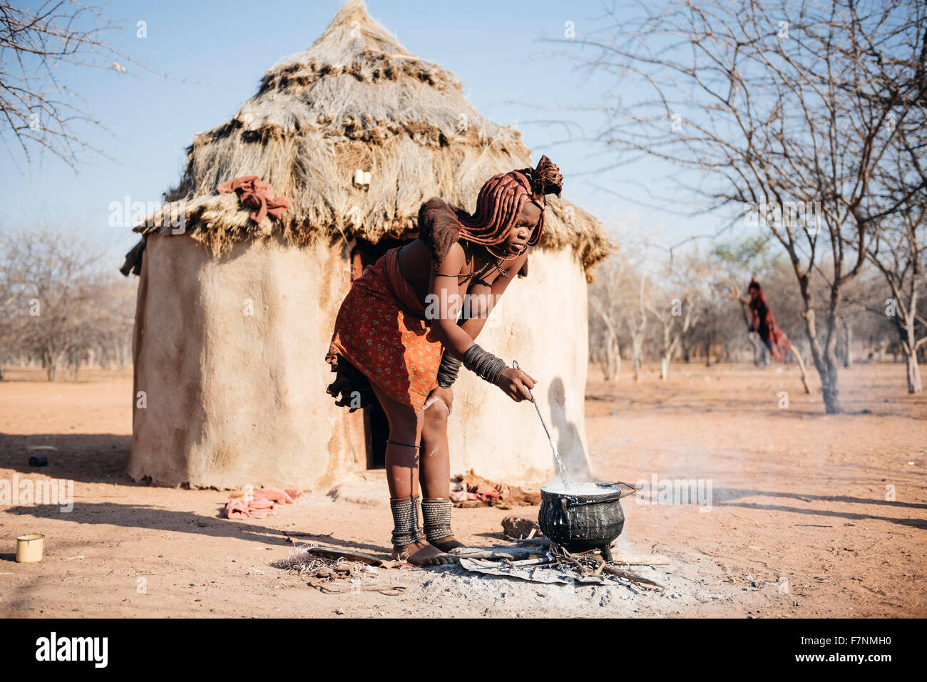 La Namibie, Damaraland, jeune femme cuisiner sur un petit feu devant sa hutte dans un village Himba Banque D'Images