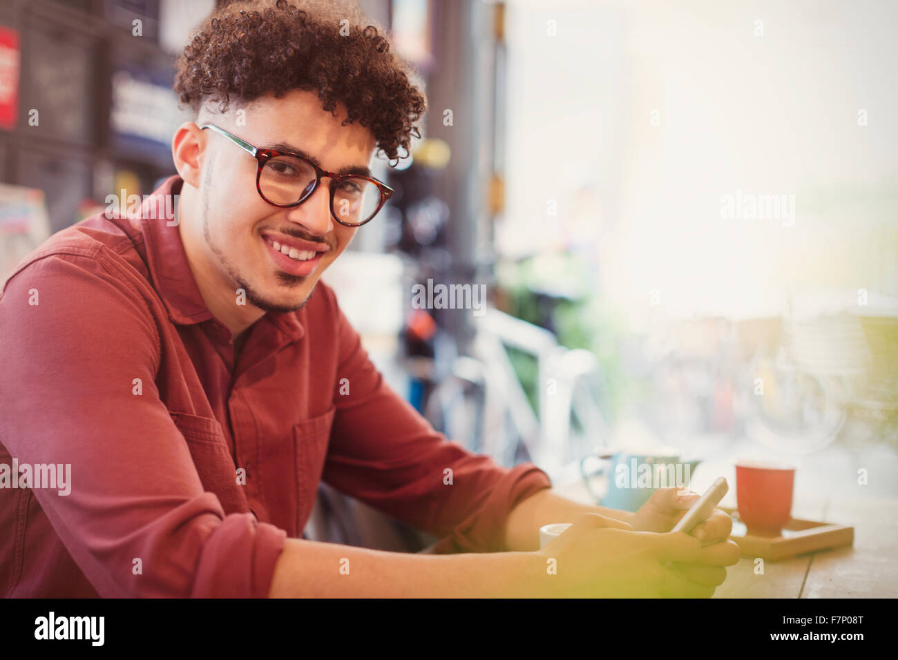 Portrait of smiling man avec les cheveux noirs bouclés texting in cafe Banque D'Images
