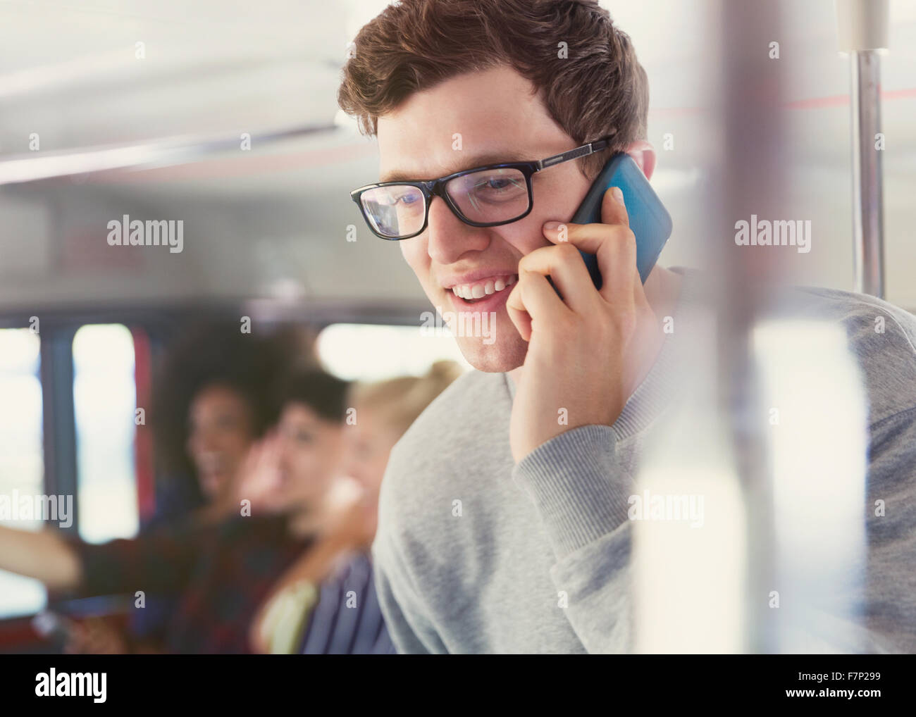 Smiling man with eyeglasses on cell phone on bus Banque D'Images