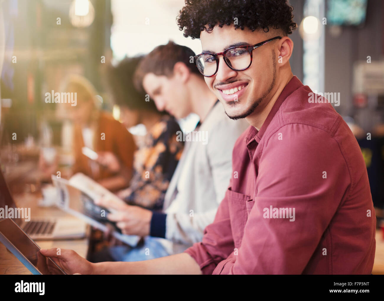 Portrait of smiling man avec les cheveux noirs bouclés using digital tablet in cafe Banque D'Images