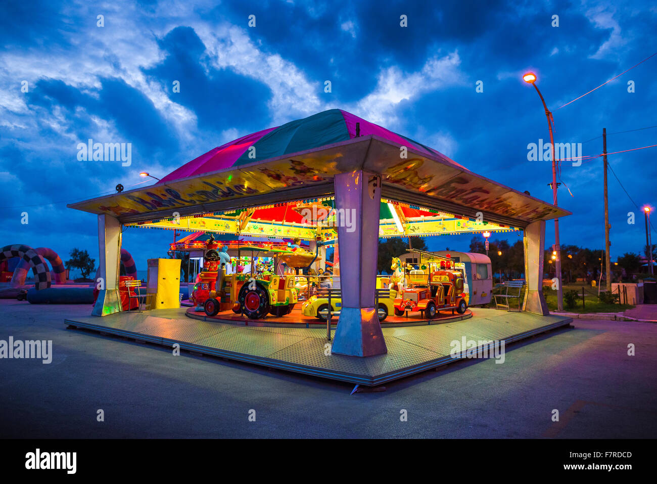 Parc d'enfants de nuit, vue d'un enfant lumineux's ride se détachant sur de sombres nuages au-dessus de la zone portuaire à Marsala, en Sicile. Banque D'Images