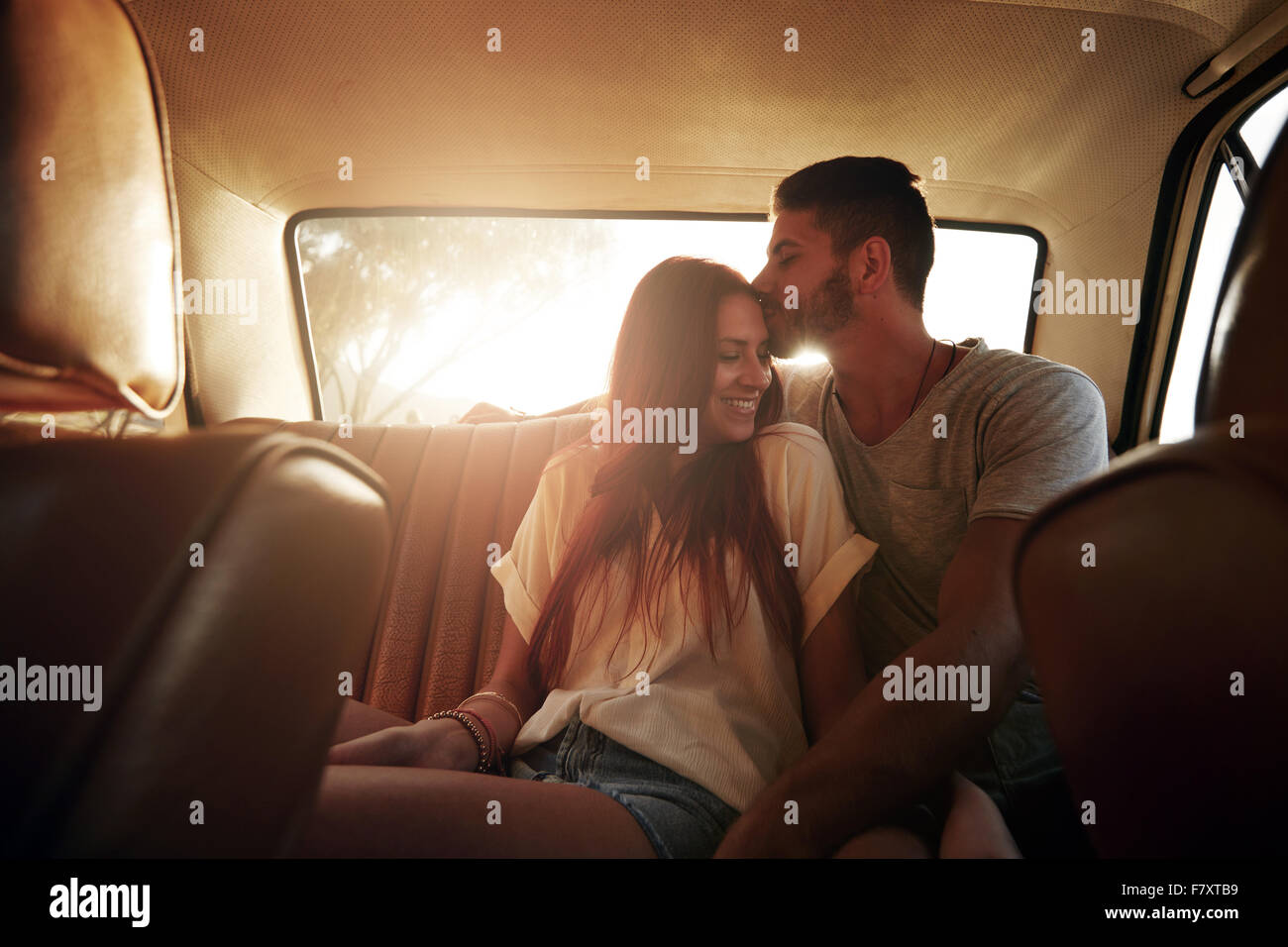 Portrait de jeune couple détendue d'un voyage assis sur siège arrière de voiture. Man kissing front de sa petite amie, avec des Banque D'Images