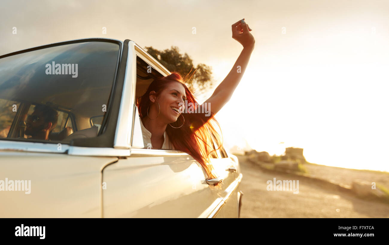 Tourné de belle jeune femme profitant de road trip sur une journée d'été. Les jeunes femmes excitées levant la main hors de la voiture. Banque D'Images
