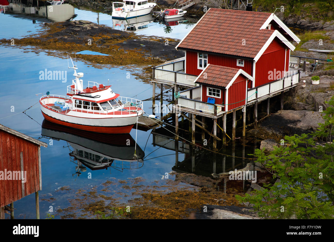 Rouge brique cabane en bois sur pilotis et petit bateau de pêche près du port des îles Lofoten Moskenes dans l'ouest de la Norvège Banque D'Images