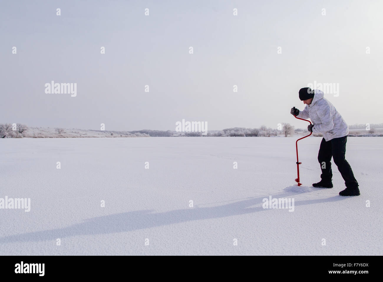 Pêcheur d'hiver avec broche à glace faire trou dans la glace sur un lac gelé Banque D'Images