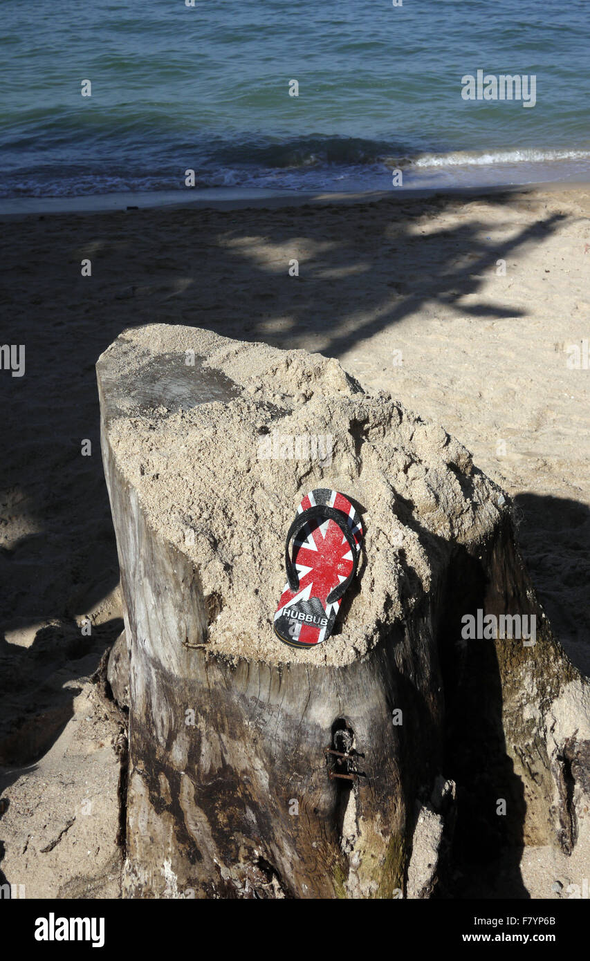 Une seule sandale avec un GO UK Union Jack Flag trouvés conception reposant sur une souche d'arbre couverts de sable sur la plage à Pattaya en Thaïlande Banque D'Images