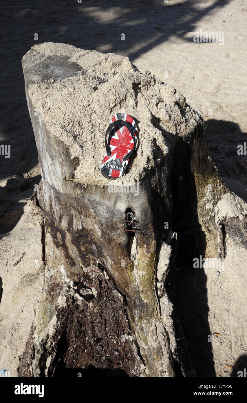 Une seule sandale avec un GO UK Union Jack Flag trouvés conception reposant sur une souche d'arbre couverts de sable sur la plage à Pattaya en Thaïlande Banque D'Images
