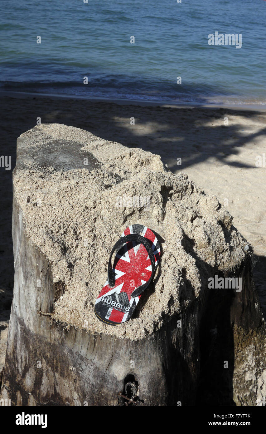 Une seule sandale avec un GO UK Union Jack Flag trouvés conception reposant sur une souche d'arbre couverts de sable sur la plage à Pattaya en Thaïlande Banque D'Images