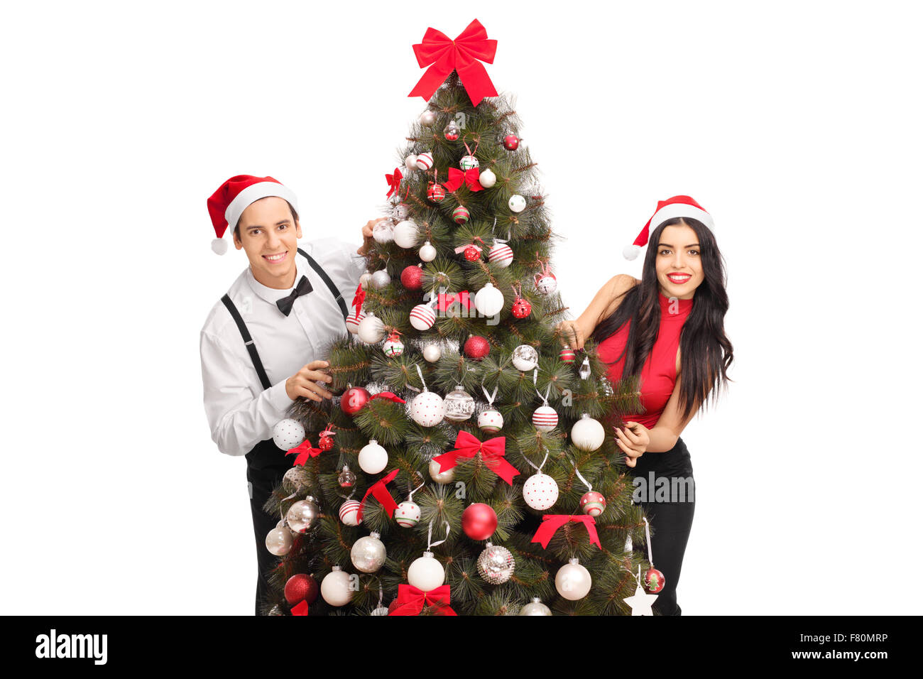 Jeune homme et femme avec Santa hats posant derrière un arbre de Noël isolé sur fond blanc Banque D'Images