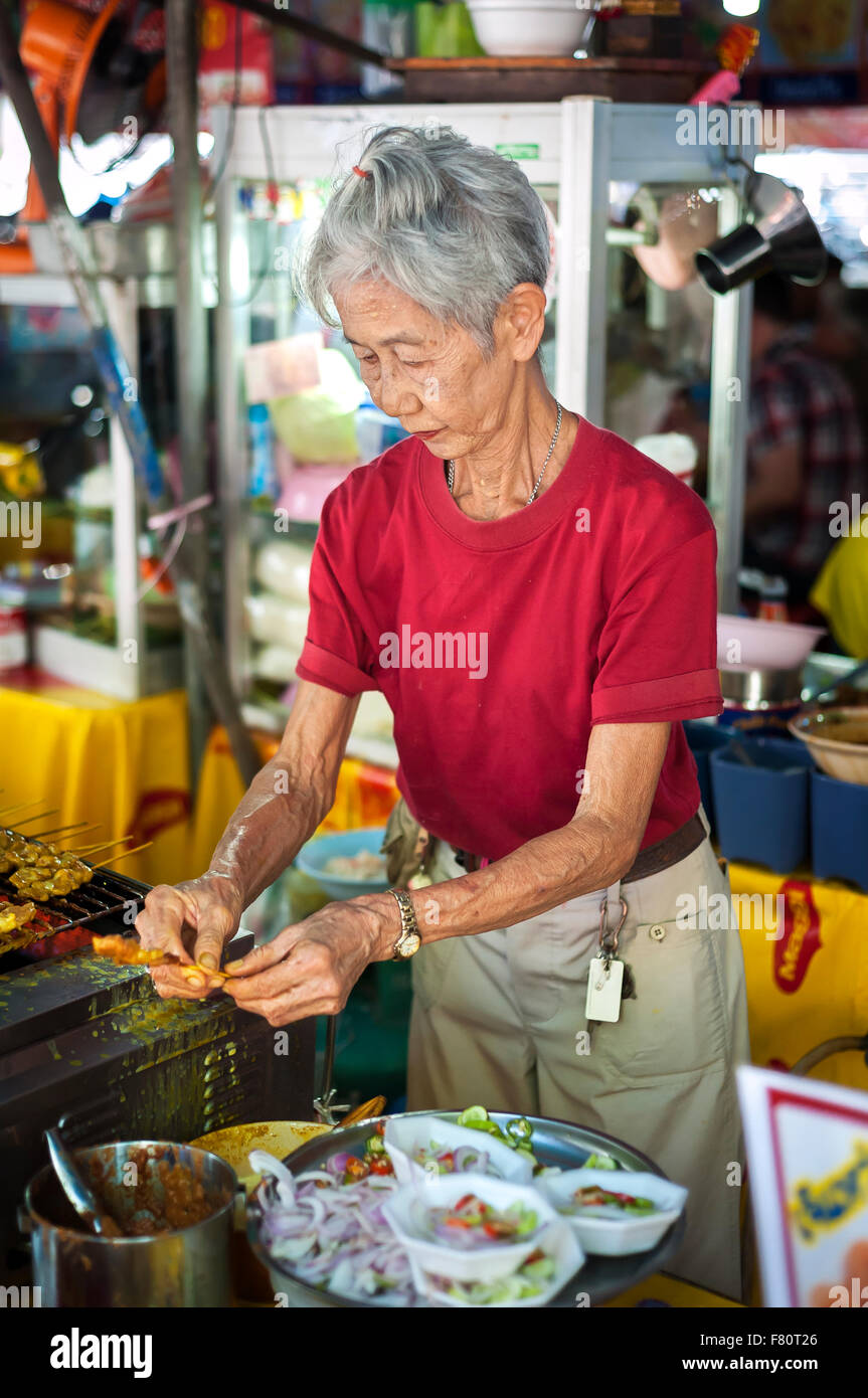 Vieille dame préparer des collations de viande à Chatuchak Weekend Market, Bangkok Banque D'Images