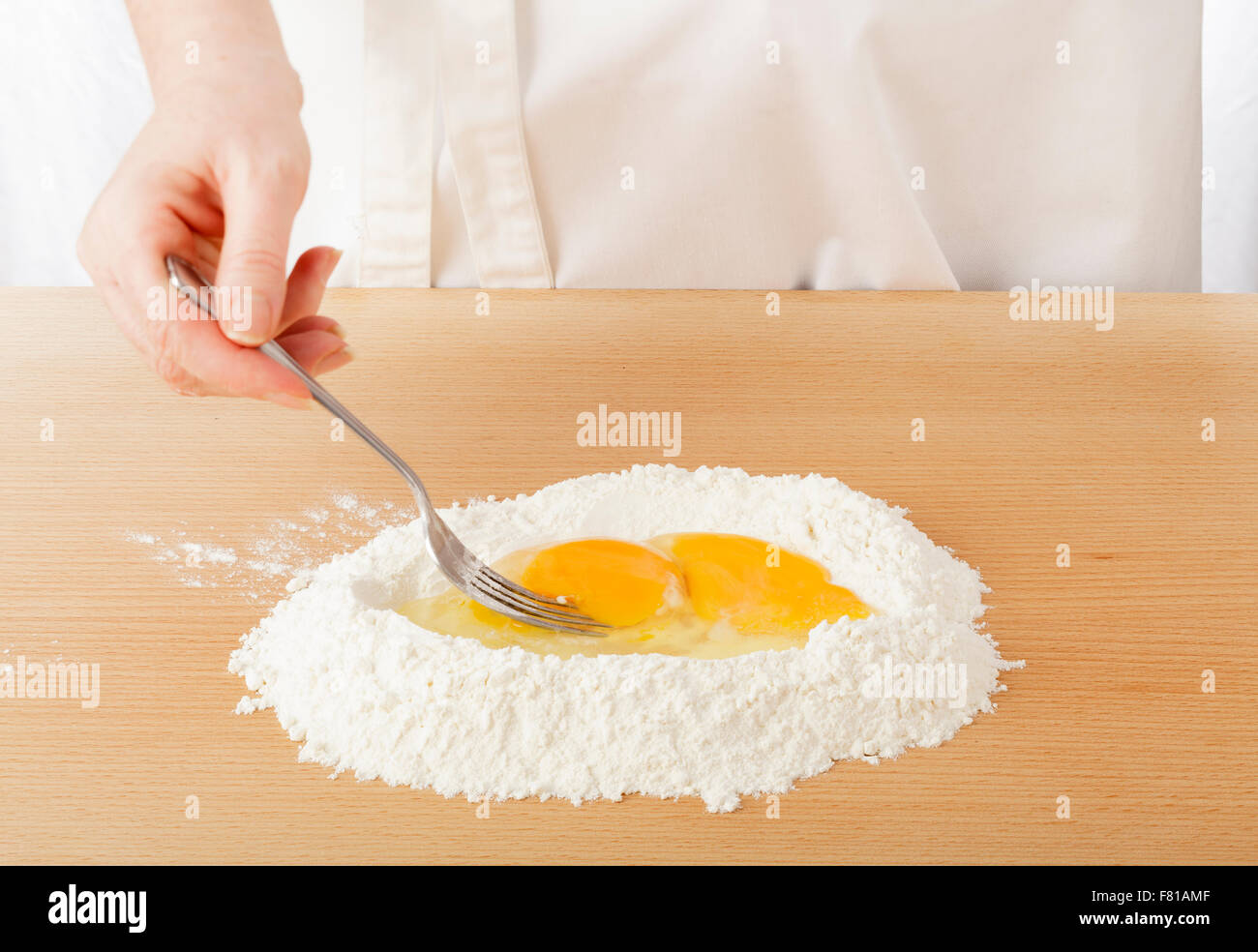 L'intérieur des œufs en fouettant chef farine sur plan de travail pour faire des pâtes Banque D'Images