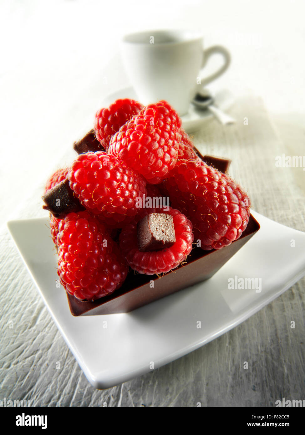 Une spécialité de pâtisserie faite à la main riche gâteau au chocolat moelleux rempli de framboises fraîches avec café dans un cadre de table blanc Banque D'Images