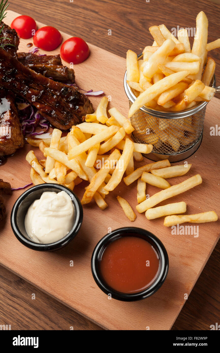 Des ailes de poulet et des côtes avec des frites sur la table en bois Banque D'Images Des ailes de poulet et des côtes avec des frites sur la table en bois Banque D'Images