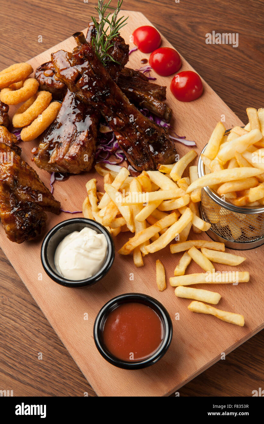 Des ailes de poulet et des côtes avec des frites sur la table en bois Banque D'Images Des ailes de poulet et des côtes avec des frites sur la table en bois Banque D'Images