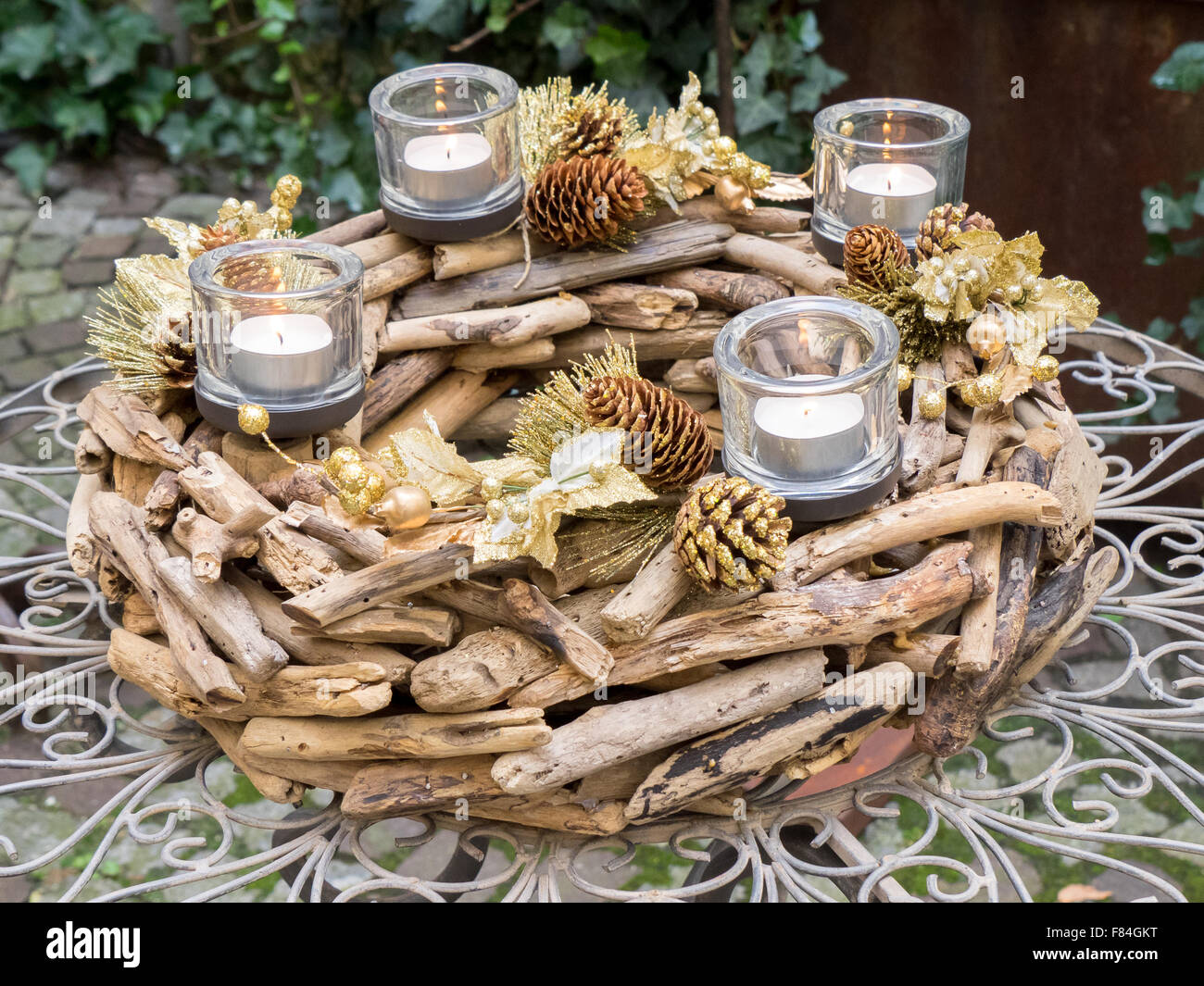 Centre de table de Noël créé avec du bois et des pommes de pin, 4 bougies, or et marron, couleurs exposées sur table de jardin. Banque D'Images