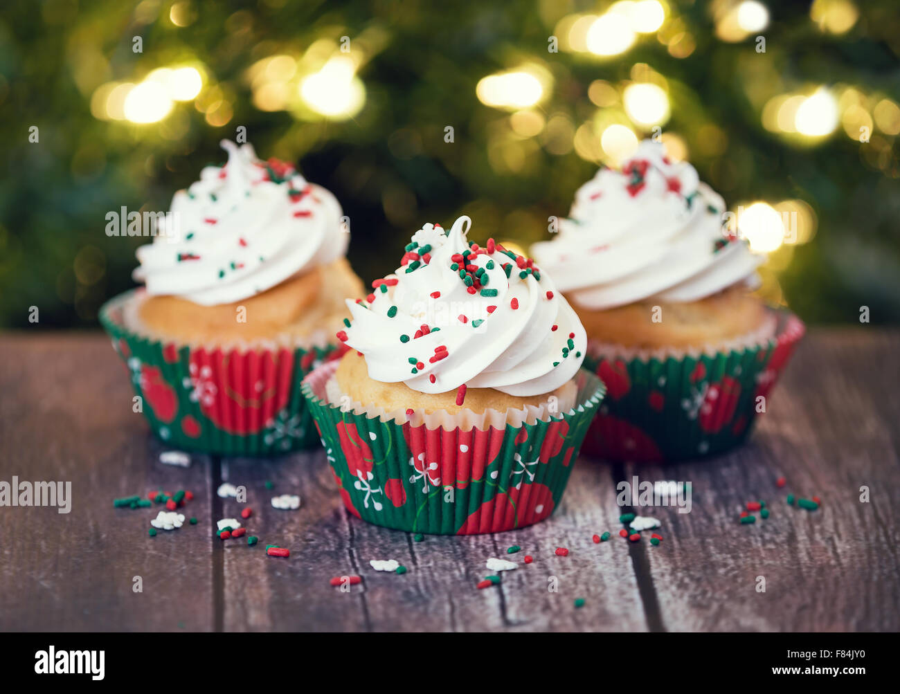 Petits gâteaux de Noël avec glaçage vanille et rouge et vert sur sprinkles table rustique Banque D'Images