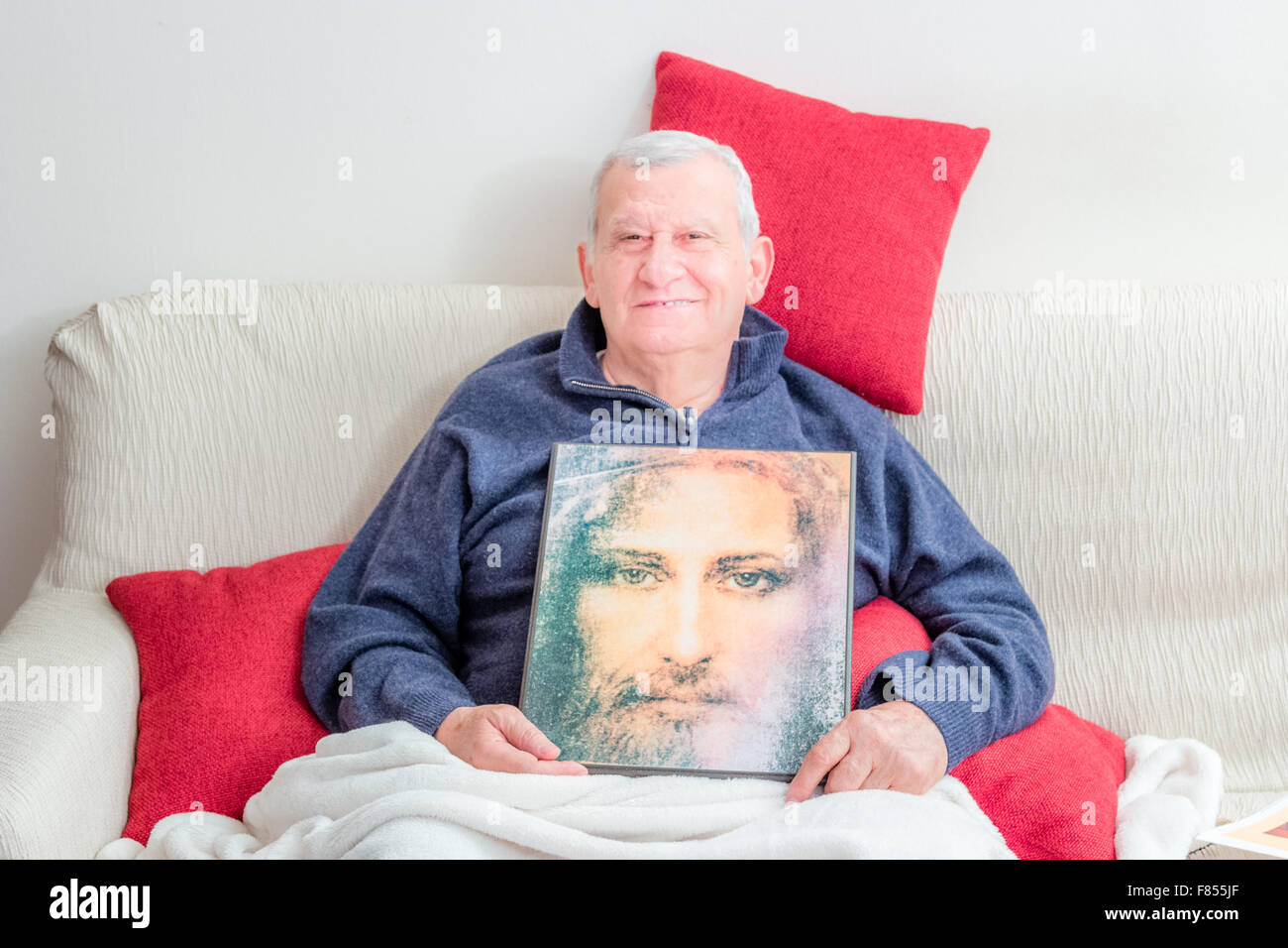 Les cadres supérieurs qui sourit alors qu'elle repose sur le canapé recouvert d'une couverture blanche et rouge des coussins et la tenue d'une icône de Jésus Christ Banque D'Images