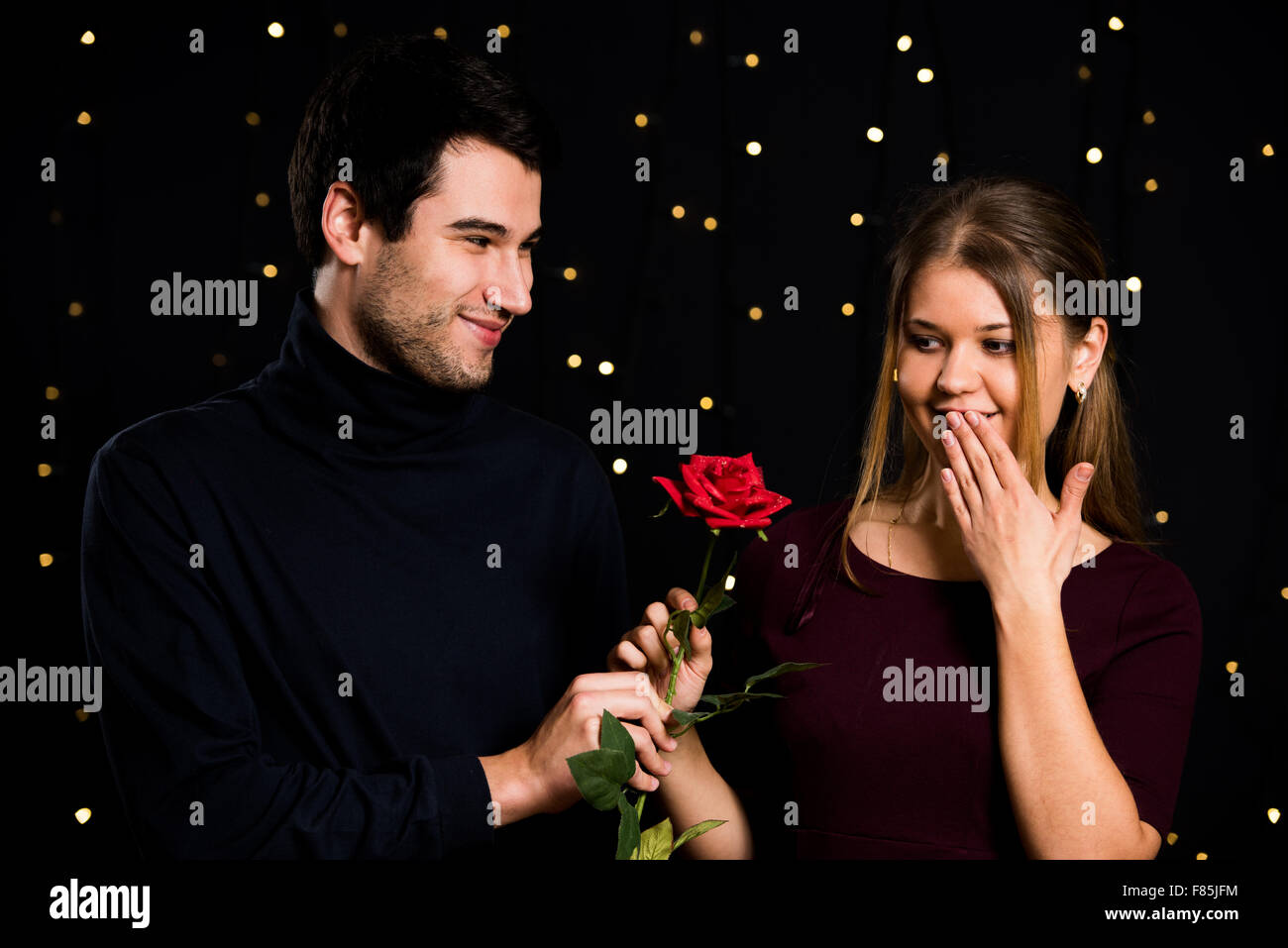 Jeune couple, homme et femme, sur fond noir, l'homme présente une rose Banque D'Images