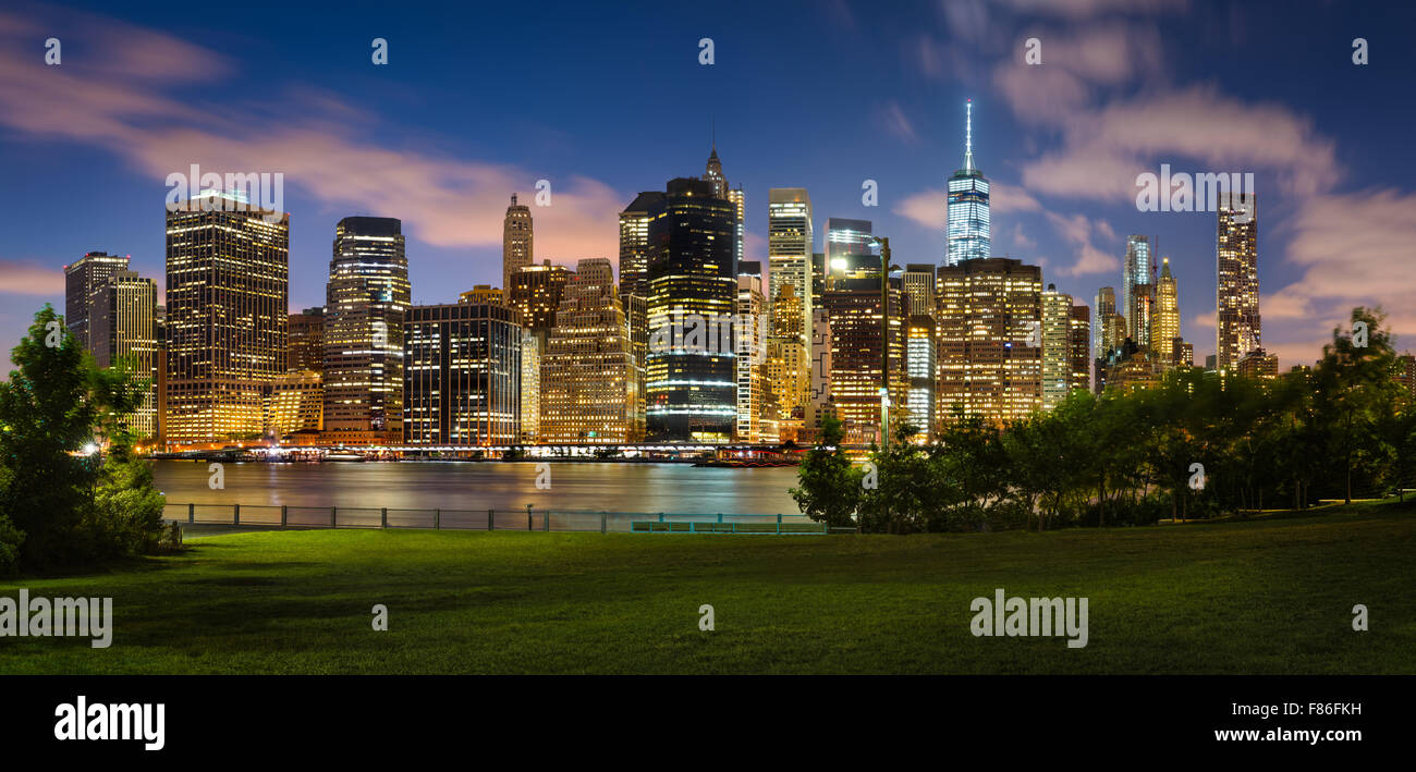 Soir vue de Lower Manhattan gratte-ciel lumineux à travers Brooklyn Bridge Park. Le Quartier Financier de Manhattan, New York City Banque D'Images