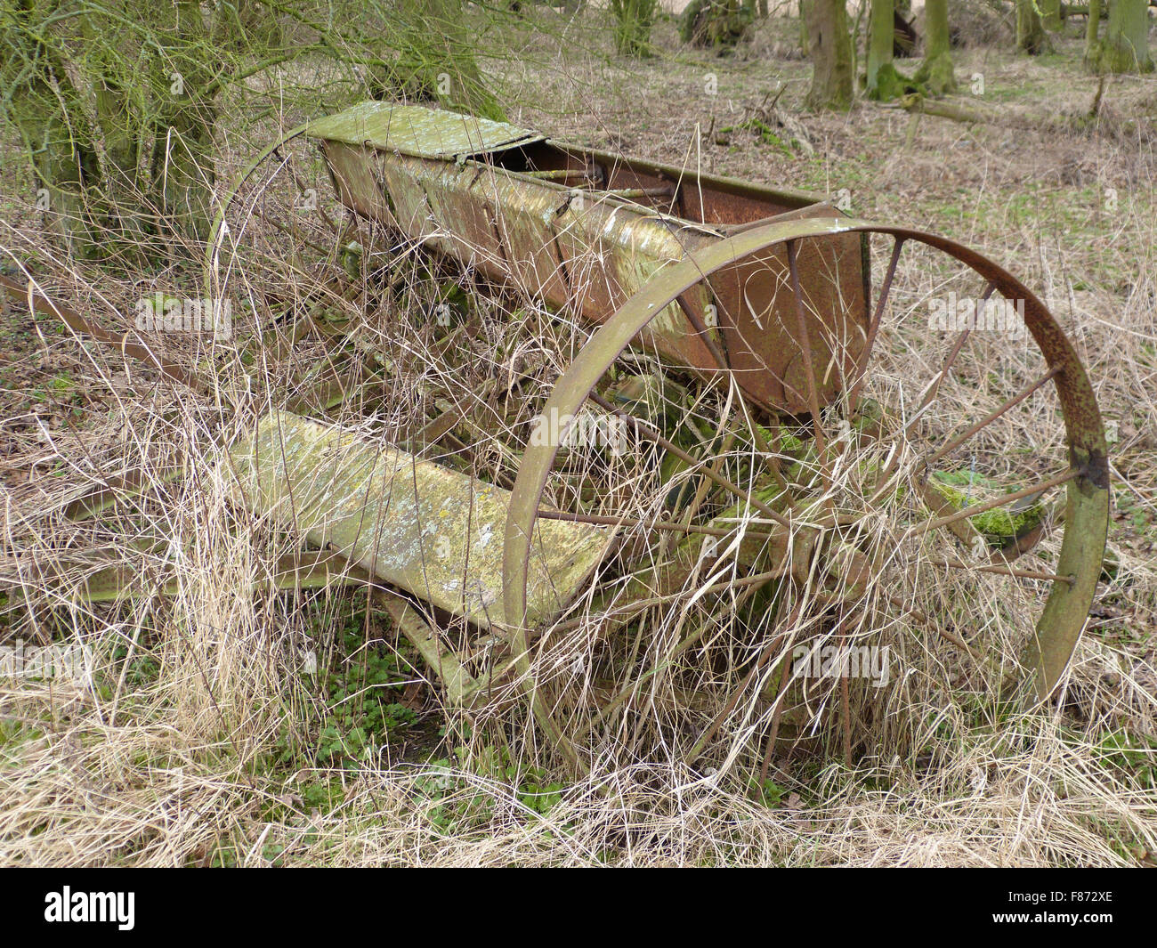 Un morceau de vieilles machines agricoles laissés à pourrir dans l'herbe haute sur une ferme dans le semoir ancien paysage roues en fonte Banque D'Images