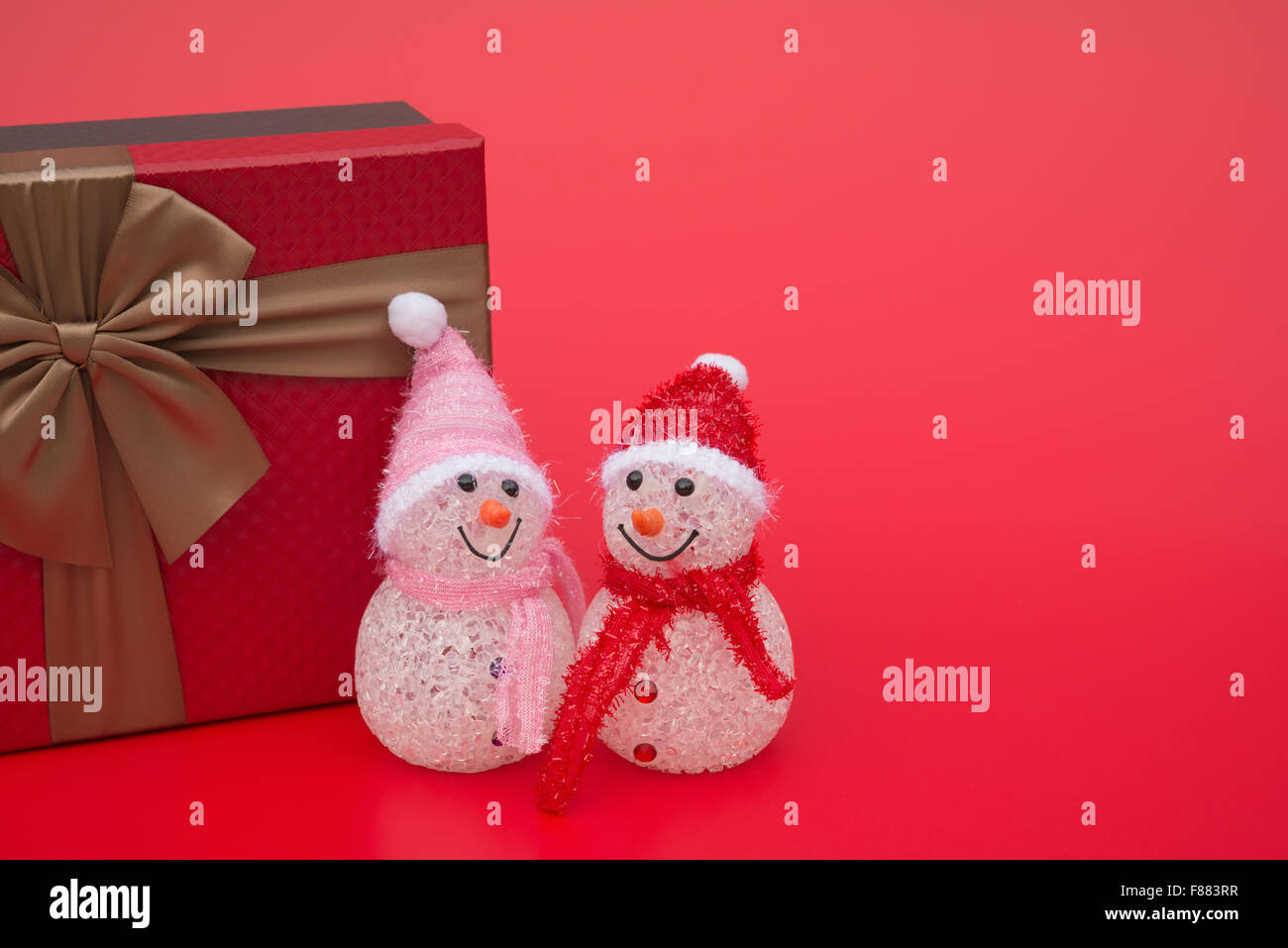 Deux smiling toy bonhomme de neige de Noël et un présent fort sur fond rouge avec copie espace Banque D'Images