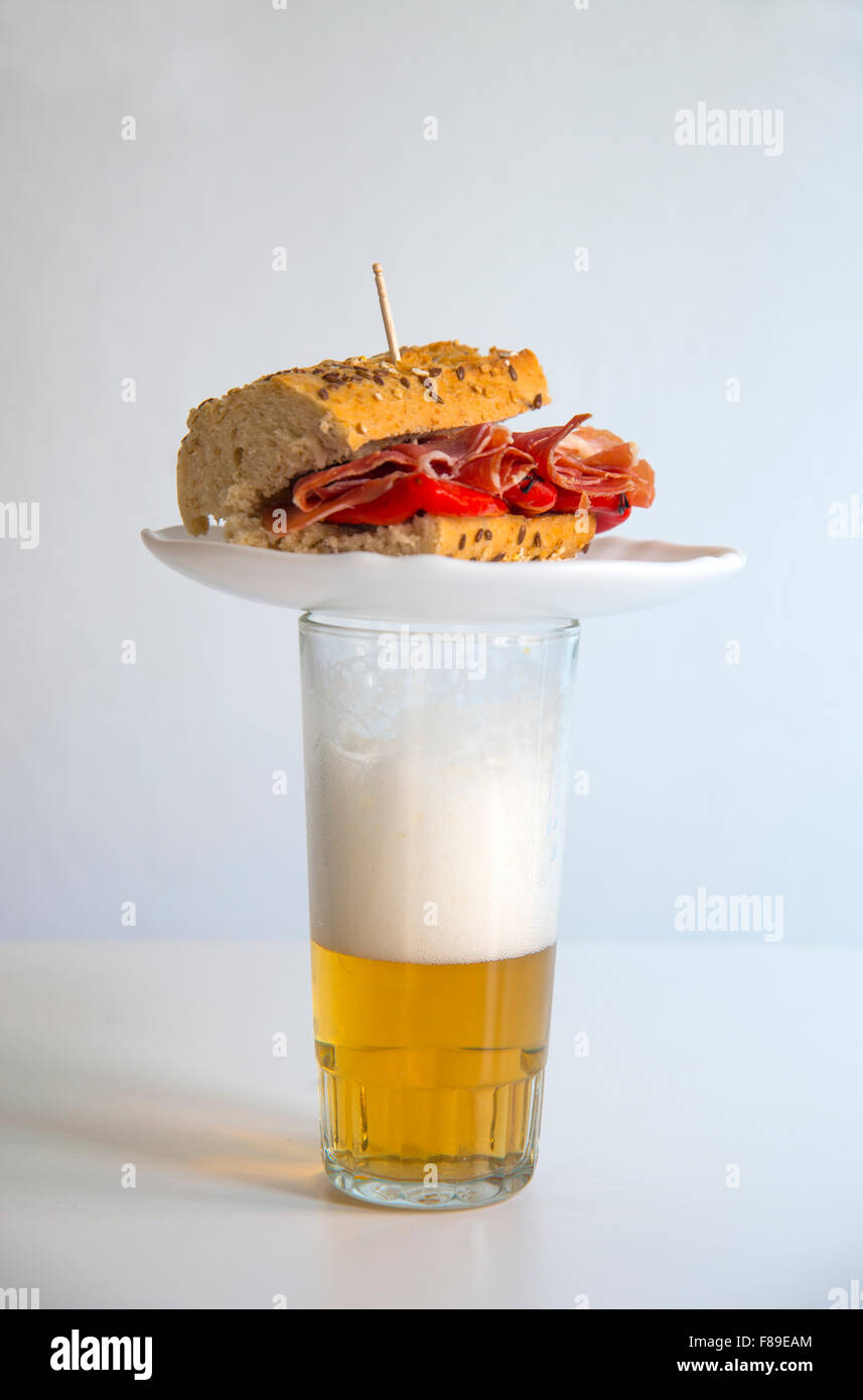 Tapa typiquement espagnol : jambon ibérique avec sandwich de poivron rouge au-dessus d'un verre de bière. Banque D'Images