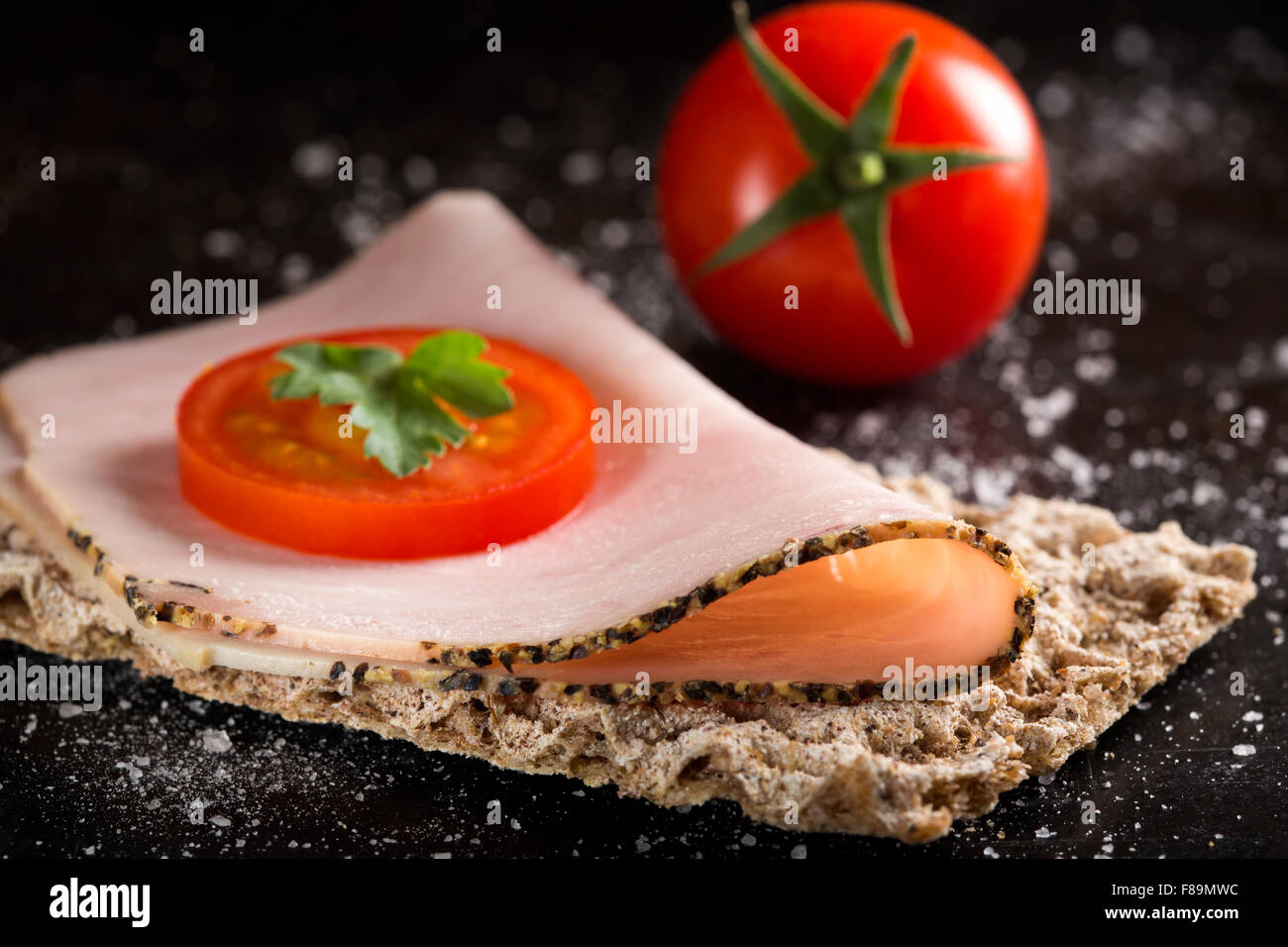 Pain croustillant au jambon et tomate sur fond sombre Banque D'Images