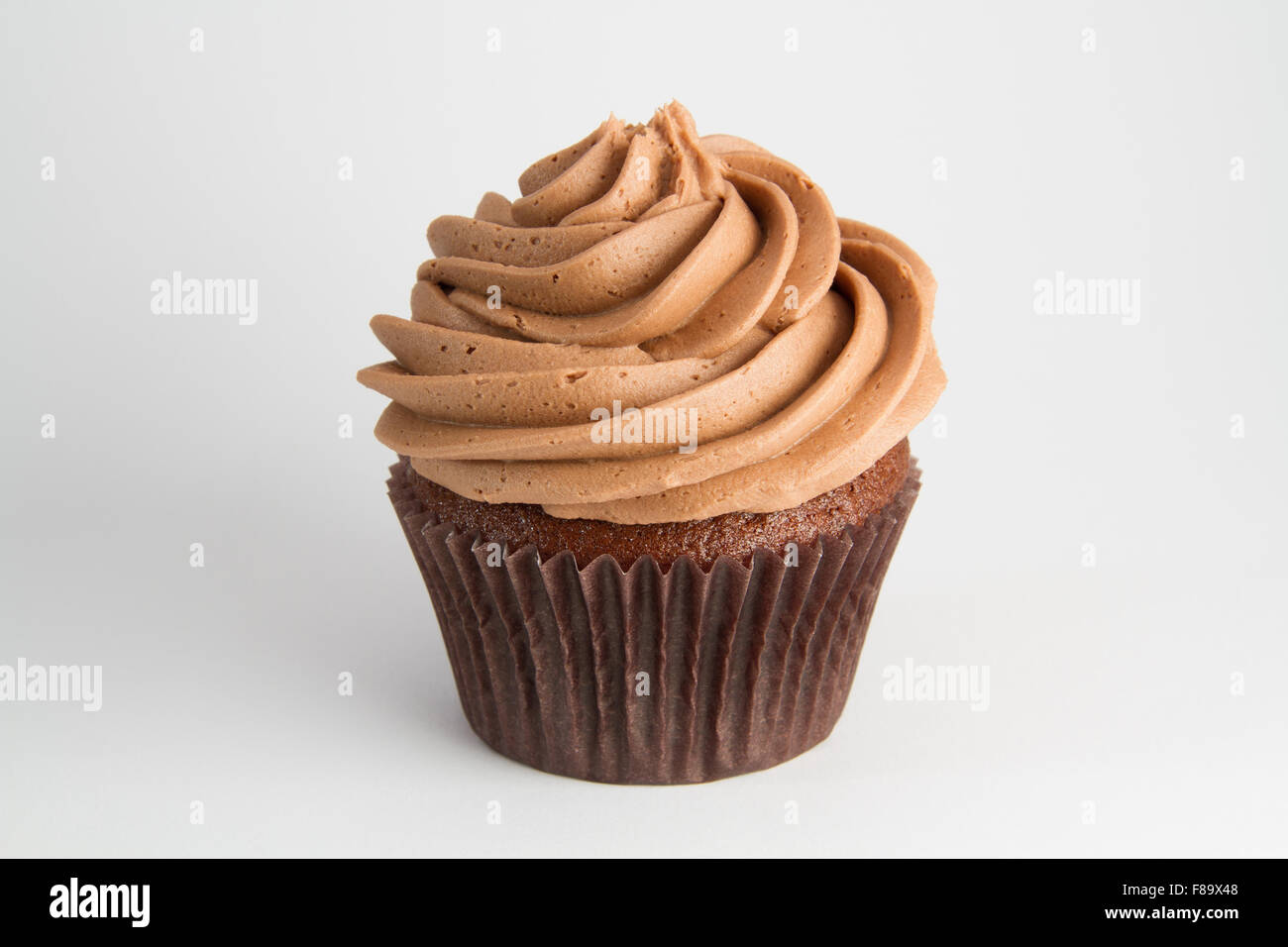 Un petit gâteau au chocolat avec glaçage tourbillonnèrent, isolé sur un fond blanc. Banque D'Images