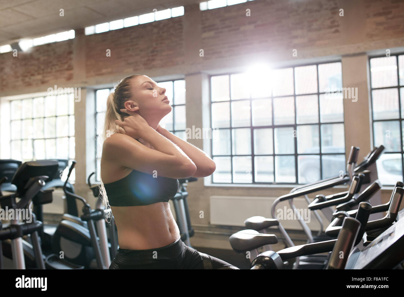 Jeune femme fatiguée après entraînement intensif sur sport moto. Les muscles de son cou se détendre après entraînement en club de remise en forme. Banque D'Images