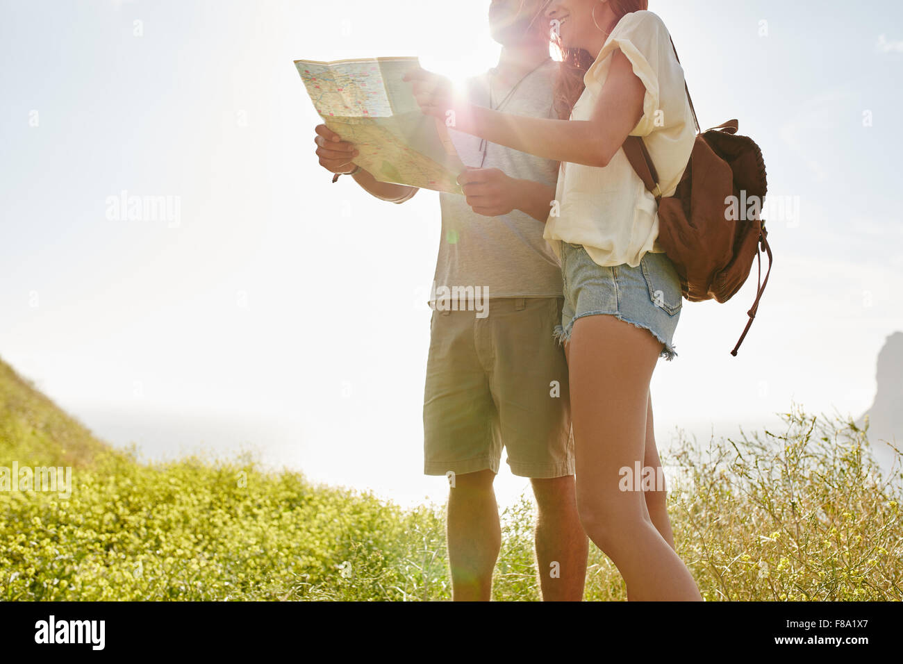 Jeune couple looking at map tout en se tenant à l'extérieur dans la campagne avec un soleil brillant de l'arrière. Couple à la directio Banque D'Images