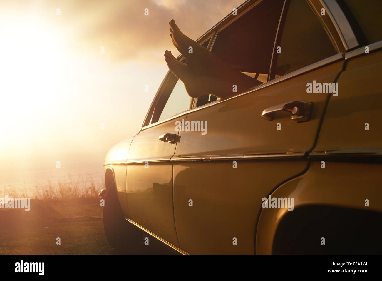 Shot of woman relaxing in a car on road trip. Pieds femelles sortir de la fenêtre du véhicule au coucher du soleil. Banque D'Images Shot of woman relaxing in a car on road trip. Pieds femelles sortir de la fenêtre du véhicule au coucher du soleil. Banque D'Images