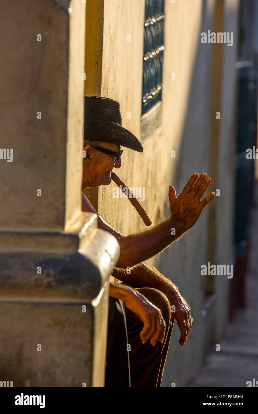 Un vieux fume un cigare cubain et assis sur un escalier dans la chaude lumière du soleil couchant, tinidad, Cuba, Santiago de Cuba, des Caraïbes, Banque D'Images