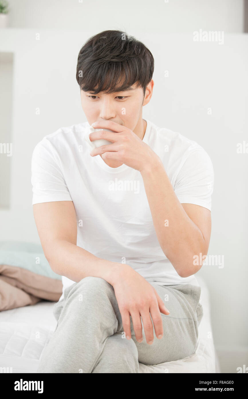 Homme assis sur le lit avec les jambes croisées et de boire une tasse de café Banque D'Images
