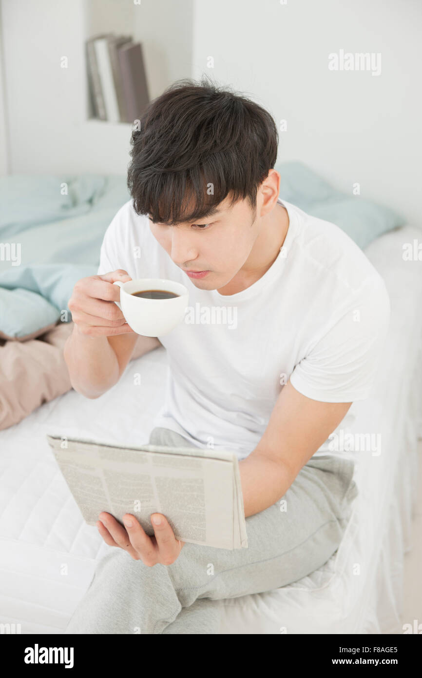 High angle de l'homme assis sur le lit de boire une tasse de café et lisant le journal Banque D'Images