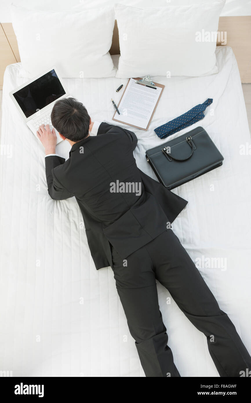 High angle d'un homme en costume d'affaires étendu sur le ventre sur le lit et de travail sur l'ordinateur portable Banque D'Images