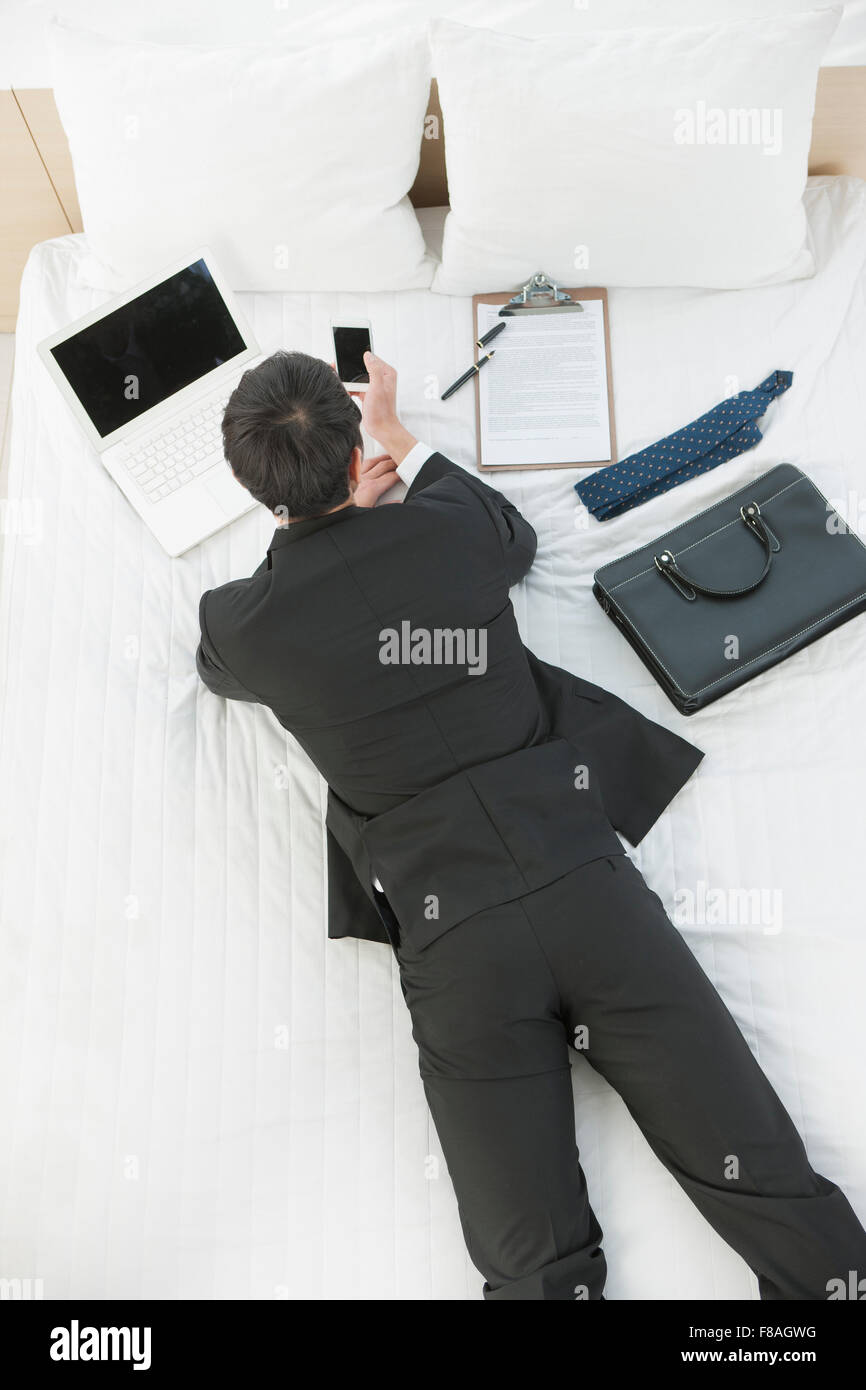 High angle d'un homme en costume d'affaires étendu sur le ventre sur le lit et en regardant le téléphone Banque D'Images