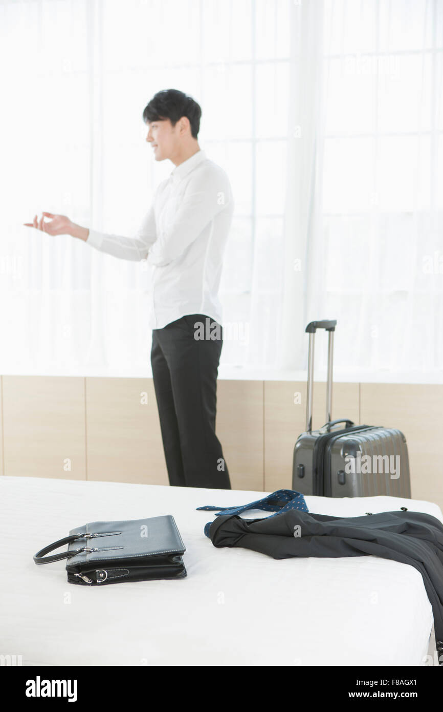 Homme debout derrière le lit avec geste de la main à côté de la valise Banque D'Images