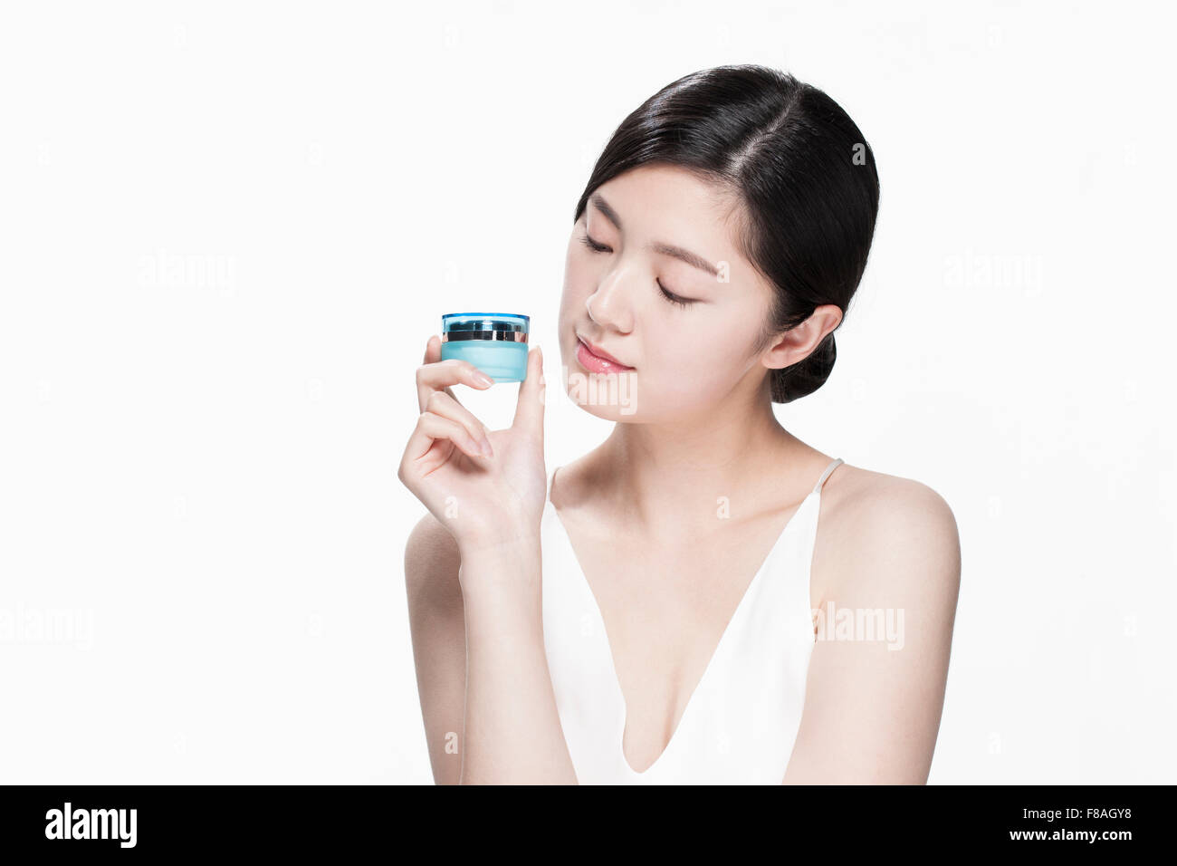 Young Asian woman looking at la crème hydratante récipient maintenu avec sa main près de son visage Banque D'Images