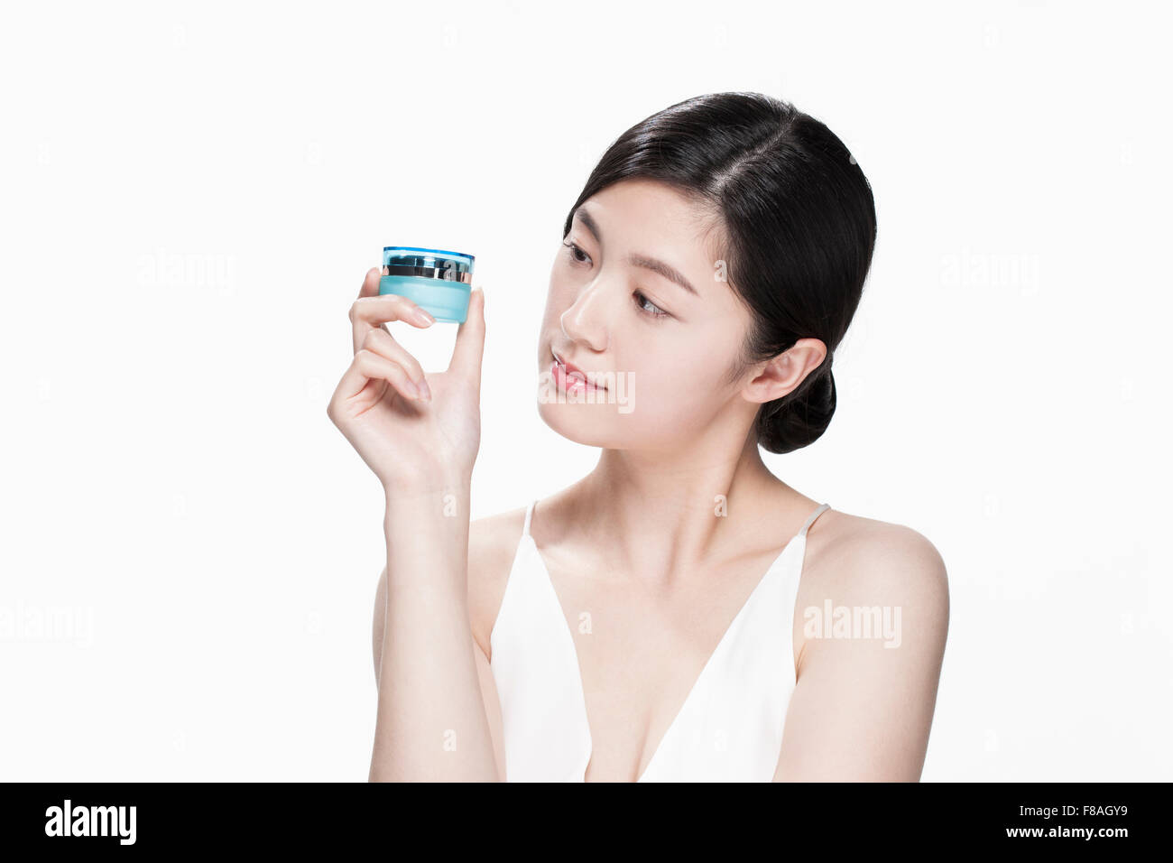 Young Asian woman looking at la crème hydratante récipient maintenu avec sa main près de son visage Banque D'Images