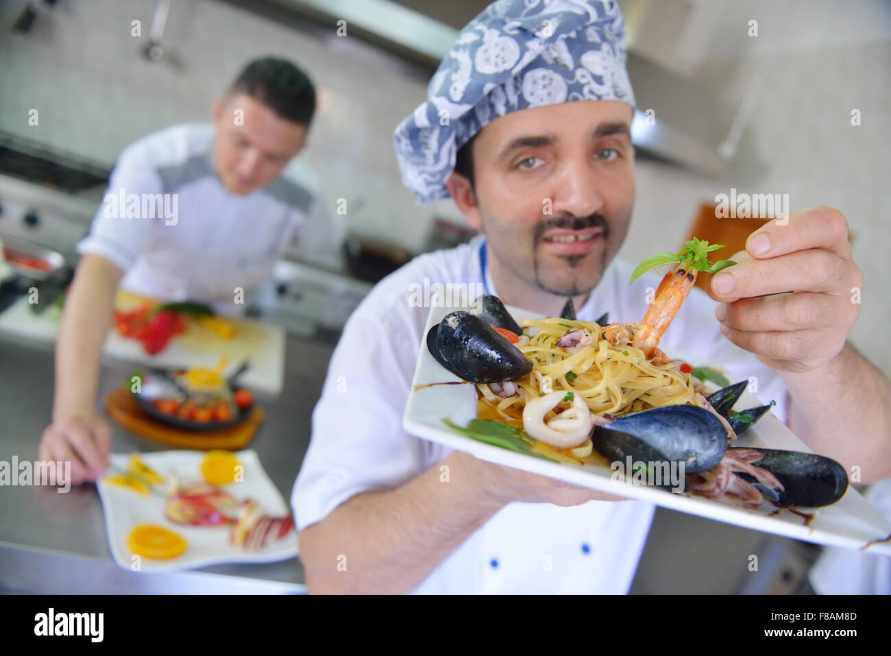 Beau chef habillé en blanc décoration uniforme de la salade de pâtes et de fruits de mer le poisson dans une cuisine moderne Banque D'Images