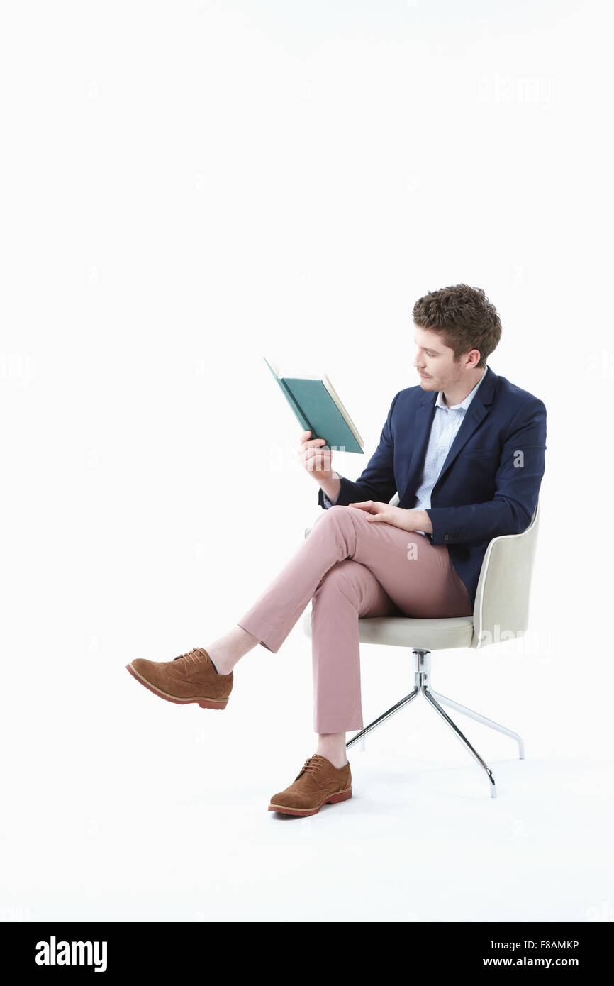 Businessman sitting on chair les jambes croisées, tenant un livre et lecture Banque D'Images