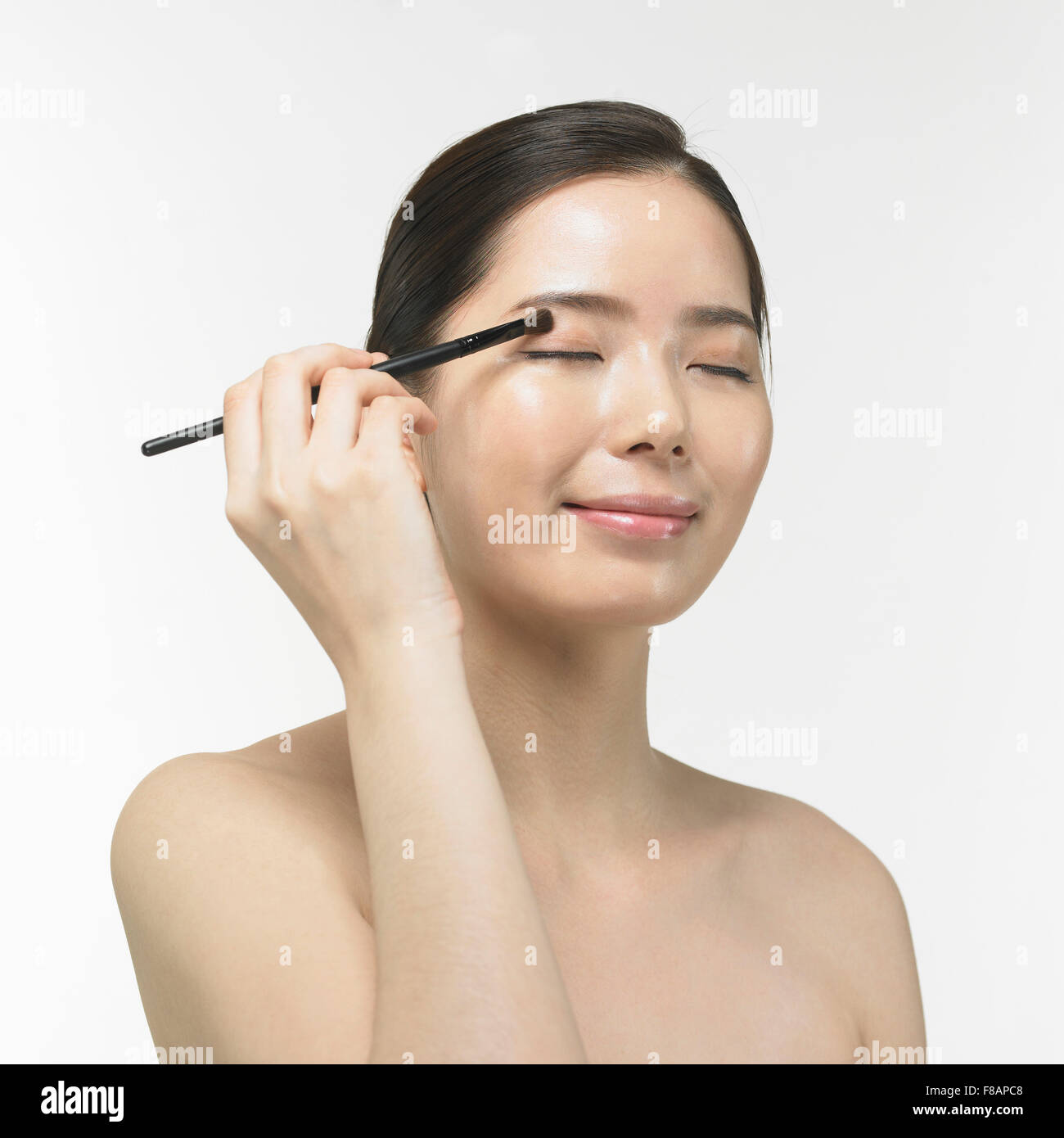 Portrait of smiling Korean woman fermant les yeux et en appliquant l'ombre d'oeil avec brosse Banque D'Images