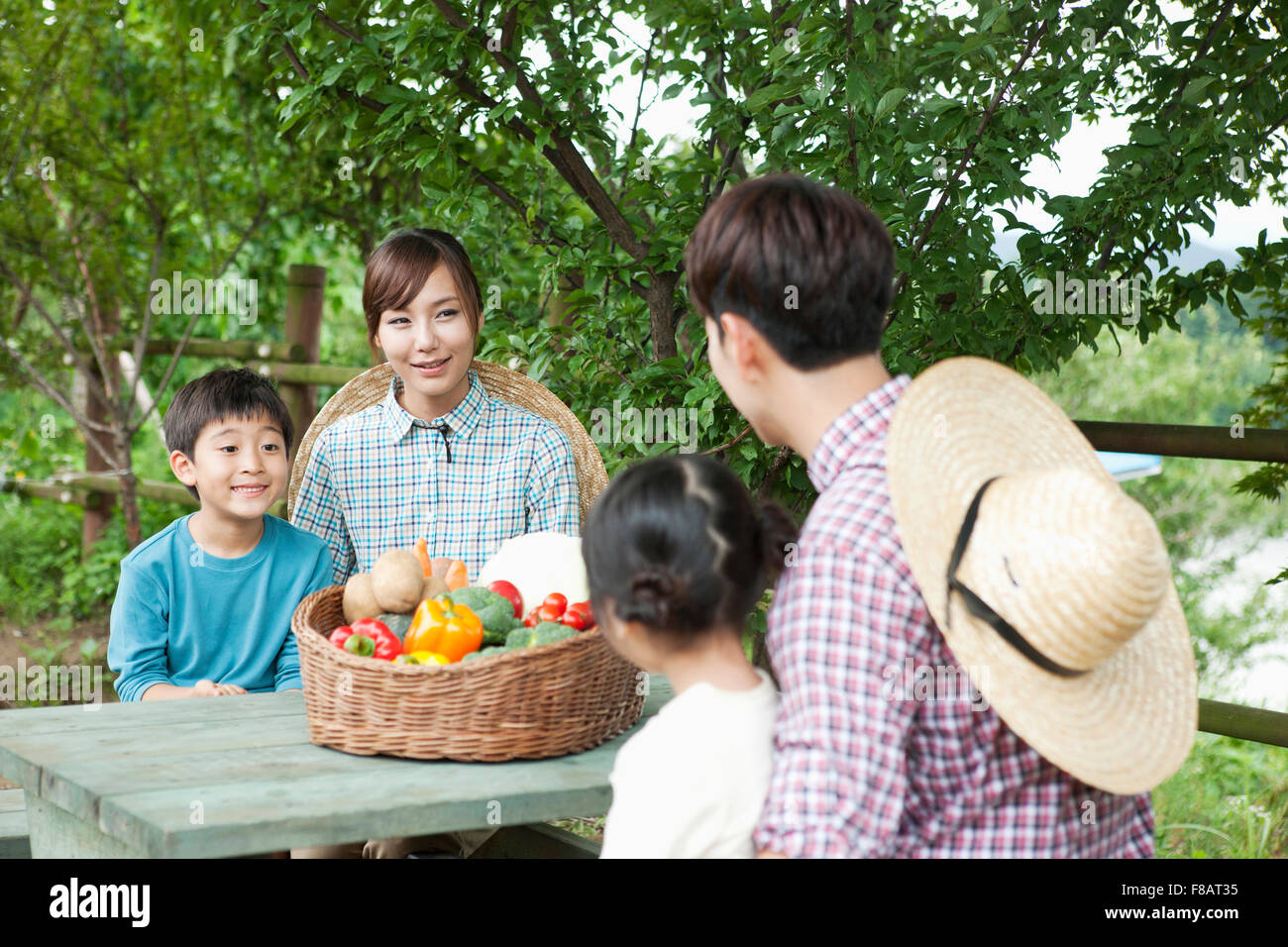 Famille aimante assis face à face à table avec des légumes frais à l'air libre Banque D'Images