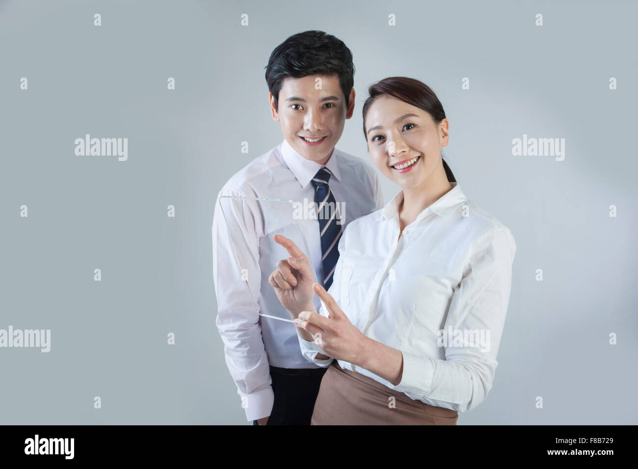 Couple dans des tenues d'affaires regardant en avant et souriant avec écran tactile dans woman's hand Banque D'Images